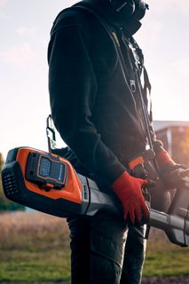 A person holding a Husqvarna product in a field during sunset.