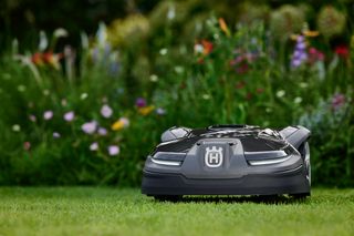 Robotic lawn mower operating in a garden with flowers in the background.