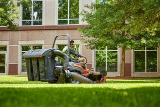 A person operating a ride-on lawn mower with a grass collection system in a landscaped area.