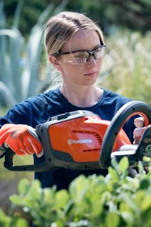 A person using a hedge trimmer to trim bushes in a garden.