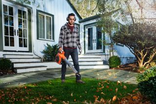 A person using a leaf blower to clear fallen leaves on a patio in a residential setting.