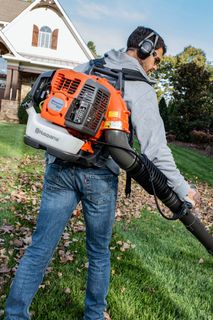 A person using a leaf blower to clear fallen leaves in a residential garden.