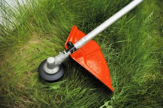 A grass trimmer cutting through tall grass in a garden setting.