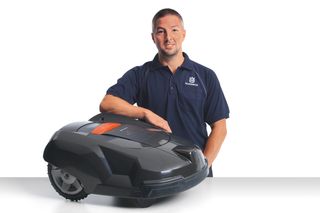 A person standing with a robotic lawn mower on a studio background.