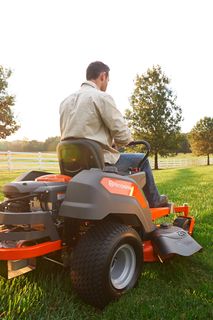 A person mowing lawn with a ride-on mower in a garden during sunset.