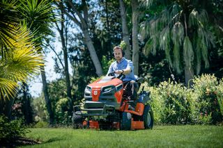 A person mowing lawn with a ride-on mower in a garden.