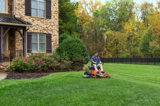 A person mowing a lawn with a ride-on mower in a residential garden.