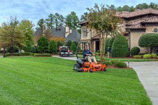 A person mowing a lawn with a ride-on mower in a residential garden setting.