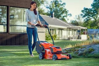 A person mowing lawn with a Husqvarna lawn mower in a residential garden setting.