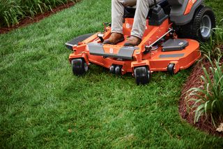 A person mowing lawn with a Husqvarna ride-on mower in a garden.