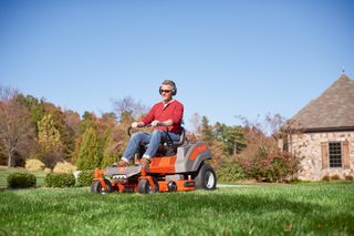 A person mowing lawn with a ride-on mower in a garden setting.