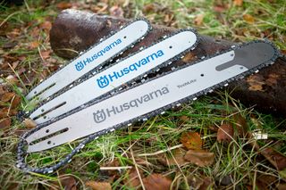 Three Husqvarna chainsaw bars placed on grass with fallen leaves.