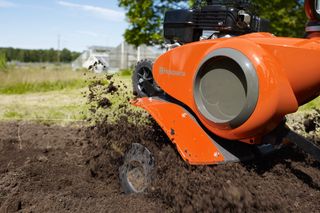 A Husqvarna tiller in action, churning soil in a garden setting.