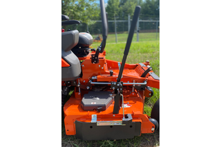 Close-up of a ride-on mower's cutting deck in a grassy area.