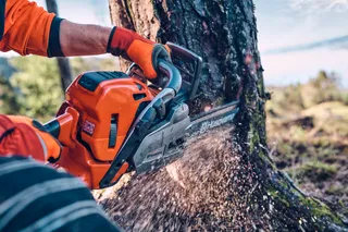 A person using a Husqvarna chainsaw to cut a tree trunk outdoors.