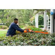 A person trimming hedges with a chainsaw in a residential garden.