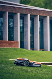 Robotic lawn mower operating on a grassy slope near a modern building.