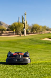Robotic lawn mower operating on a golf course with desert landscape in the background.