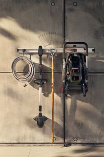 Gardening tools including a hose, rake, and lawn mower hanging on a wall rack.
