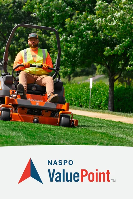 A person mowing lawn with a ride-on mower in a park setting.