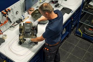 A person working on a robotic lawn mower in a workshop setting.