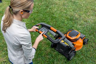 A person operating a lawn mower, adjusting settings on the control panel in a garden.
