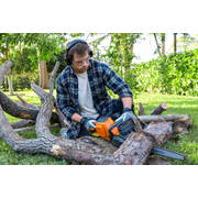 A person using a chainsaw to cut tree branches in a garden setting.