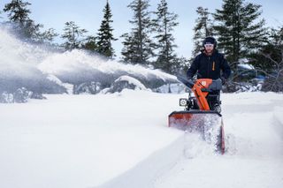 A person operating a snow blower to clear a path in a snowy landscape.