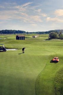 A person playing golf on a course with a robotic lawn mower maintaining the green.