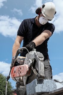A construction worker using a power cutter to cut stone outdoors, wearing protective gear.