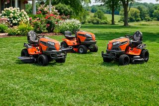 Three Husqvarna ride-on mowers parked on a lawn in a garden setting with trees and flowers.